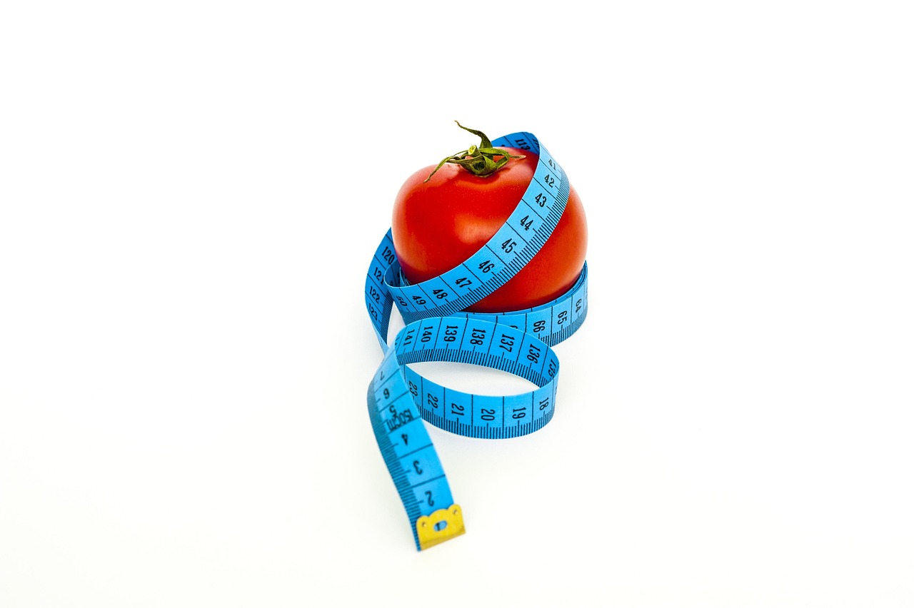 Pomidor owinięty niebieską miarką krawiecką symbolizujący liczenie kalorii i dietę.